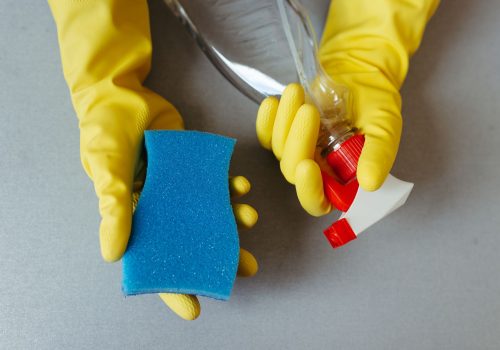 Manos con guantes sosteniendo una esponja y un pulverizador de limpieza
